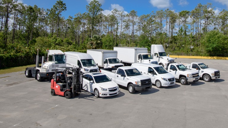 A mixed fleet of sedans, pickups, vans, box trucks, a yard tractor and a forklift on an FLD lot